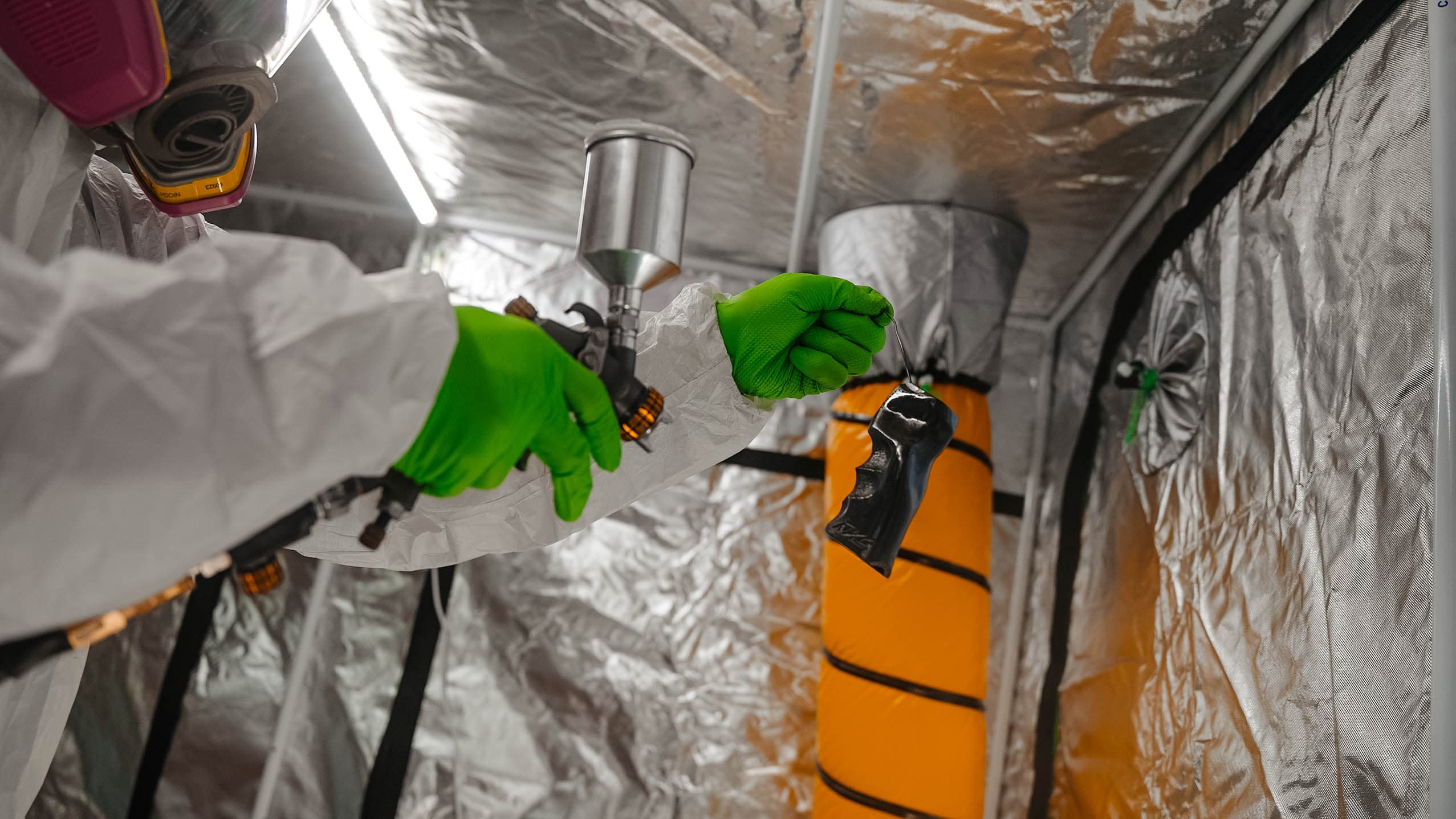 Technician applying Cerakote finish to a firearm grip in a spray booth